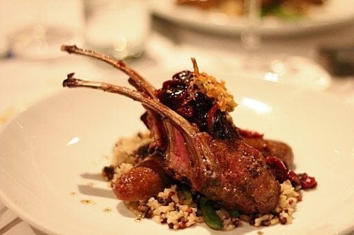 a lamb duo in a plate, composed of roasted rack of lamb with merguez sausage, black pearl medley and wild blackberry chutney
