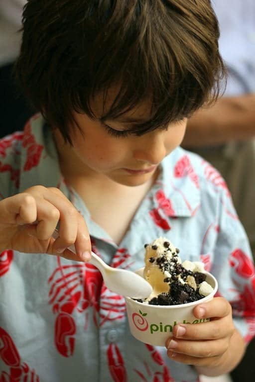 little boy holding a cup frozen yogurt topped with chocolate