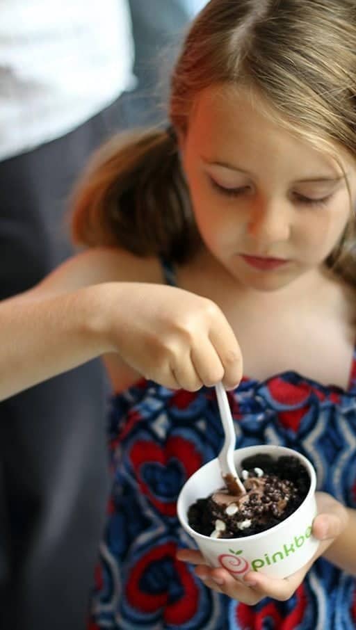 little girl scooping a frozen yogurt from the cup she's holding