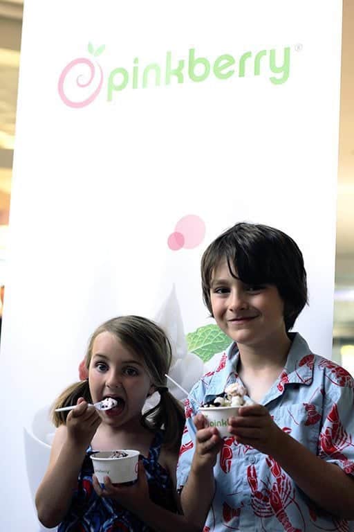two kids holding their cup of frozen yogurt with the Pinkberry wall background