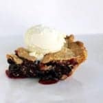 close up a slice of Rhubarb Saskatoon Pie topped with a scoop of vanilla ice cream