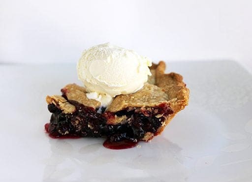close up a slice of Rhubarb Saskatoon Pie topped with a scoop of vanilla ice cream