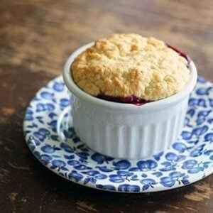 Old Fashioned Saskatoon Cobbler in a white ramekins with biscuit topping placed on a blue saucer plate