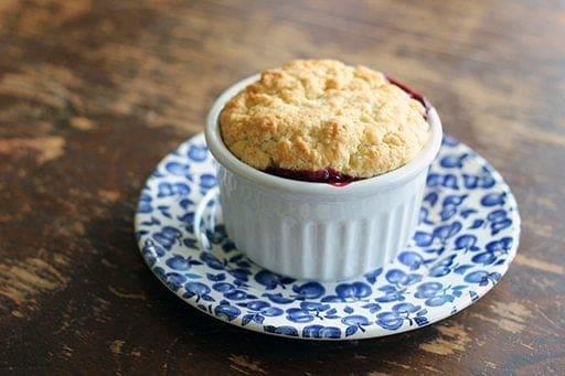 Old Fashioned Saskatoon Cobbler in a white ramekins with biscuit topping placed on a blue saucer plate