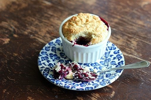 a spoon of rich Saskatoon berry filling with the cakey biscuit topping on blue saucer plate beside white ramekins