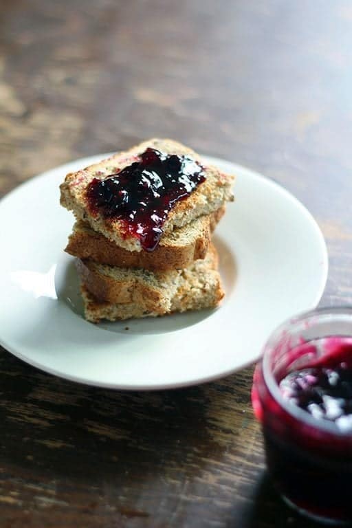 close up of Saskatoon Berry Jam on top of toast in a white plate and on a jar beside it