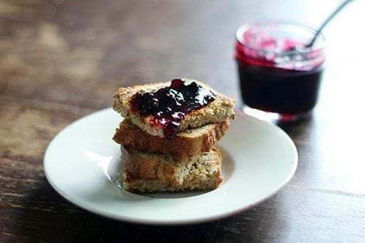 A stack of toast with traditional saskatoon berry jam on top in a white plate. A jar of saskatoon berry jam in a jar on the background.