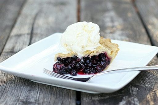 a slice of Saskatoon berry pie topped with a scoop of vanilla ice cream in a white plate