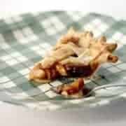 A slice of lattice-topped apple pie sits on a green-and-white plaid plate, with a spoon holding a small bite of the pie on the side.
