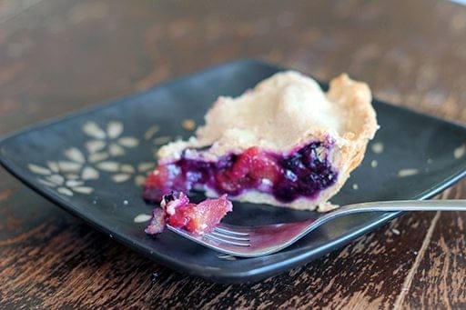 slice of Blueberry Peach Pie in a black plate with a piece of blueberry in a fork