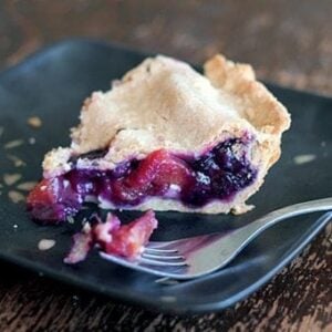 slice of Blueberry Peach Pie in a black plate with a piece of blueberry in a fork