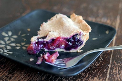 slice of Blueberry Peach Pie in a black plate with fork on wood background