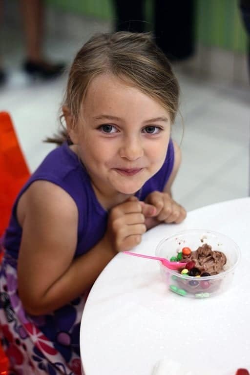 a cup of frozen yogurt with chocolate candies in front of a little girl