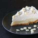 black plate with a slice of White Chocolate Cream Pie garnish with white chocolate chips