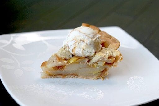 close up slice of Pear Pie in a white plate topped with a scoop of ice cream