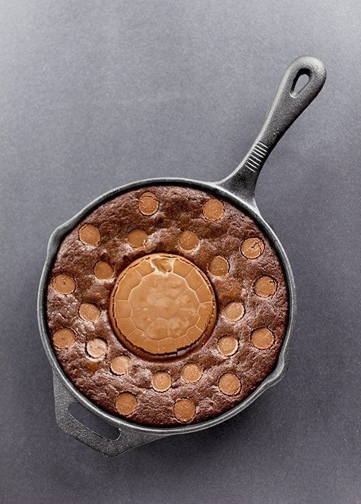 half pound giant Reese's Peanut Butter cup in the middle of a skillet, surrounded with chewy brownie batter and more baby peanut butter cups