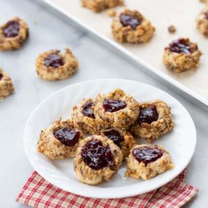 freshly baked Raspberry Walnut Thumbprint Cookies in a white plate and in parchment lined baking sheets