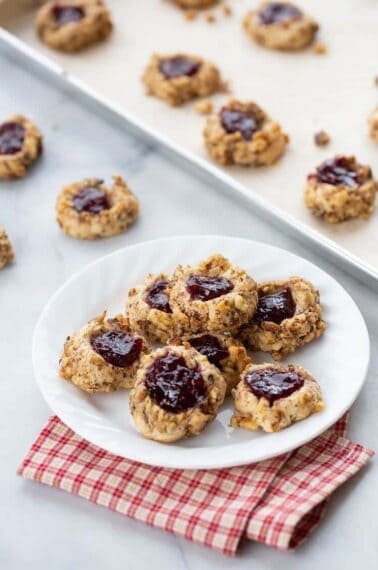 freshly baked Raspberry Walnut Thumbprint Cookies in a white plate and in parchment lined baking sheets