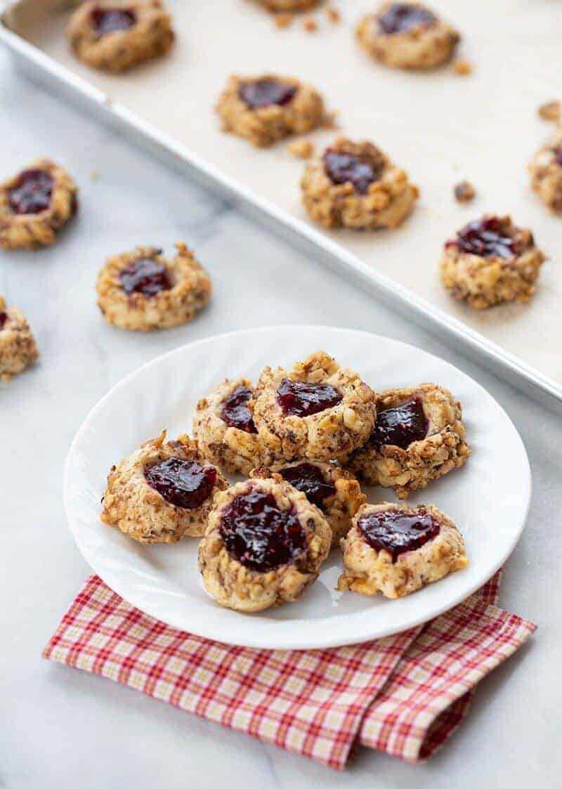 freshly baked Raspberry Walnut Thumbprint Cookies in a white plate and in parchment lined baking sheets