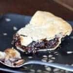 close up of a slice of mincemeat pie in a black plate with a spoon
