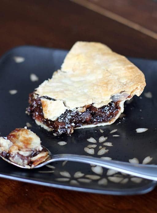 close up of a slice of mincemeat pie in a black plate with a spoon 