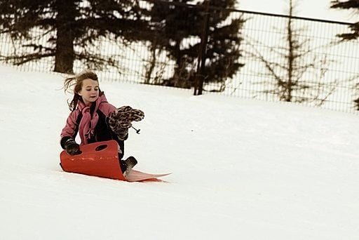 young girl holding her winter hat while in the red sled
