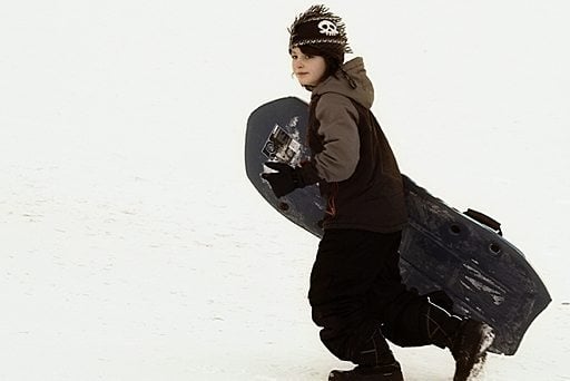 young boy walking in the snow with his sled