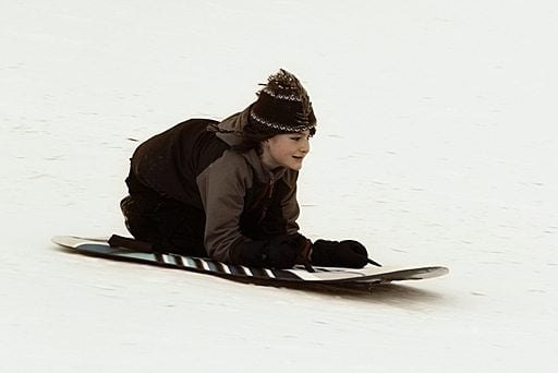 young boy sledding over snow