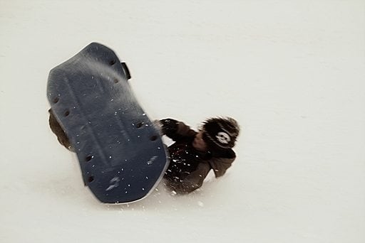 young boy enjoys sledding over snow