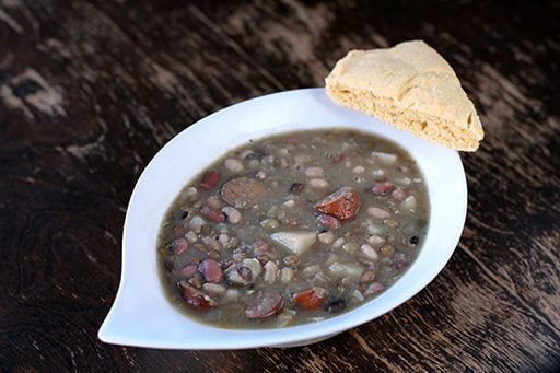 Bean, Potato and Sausage Soup in a White Soup Bowl with a slice of bread on side 