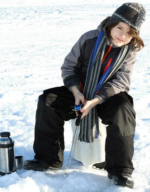 young boy sitting while his fishing rod on the hole for fishing