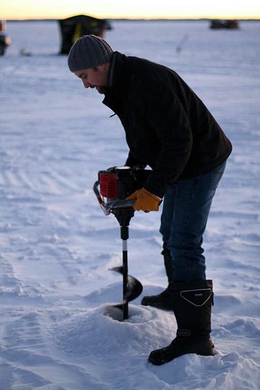 man creating hole for ice fishing