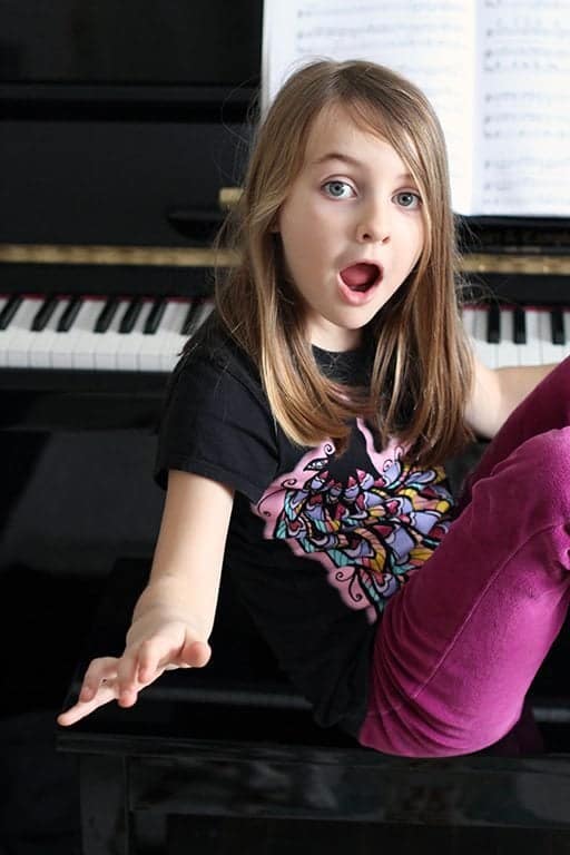 close up of young girl sitting in front of piano with her wacky face