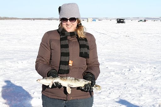 woman wearing brown coat holding a small Northern Pike