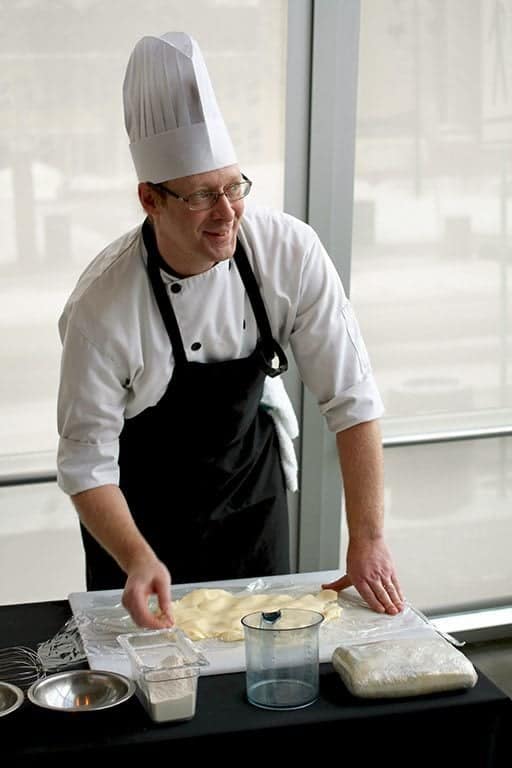 chef in his uniform holding the rolled out dough in the table