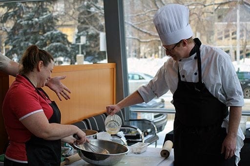 chef pouring liquid mixture to the mixing bowl while a woman holds it