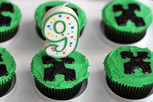 cupcakes with green buttercream icing and drawing of creeper faces on middle, number 9 candle in one of the cupcakes