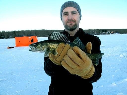 man wearing a black coat and beanie hat holding a baby walleye fish