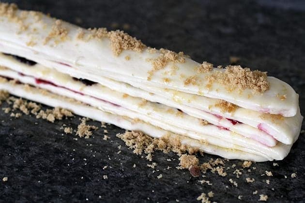 stack of dough strips with sprinkled sugar and halves cherry in between