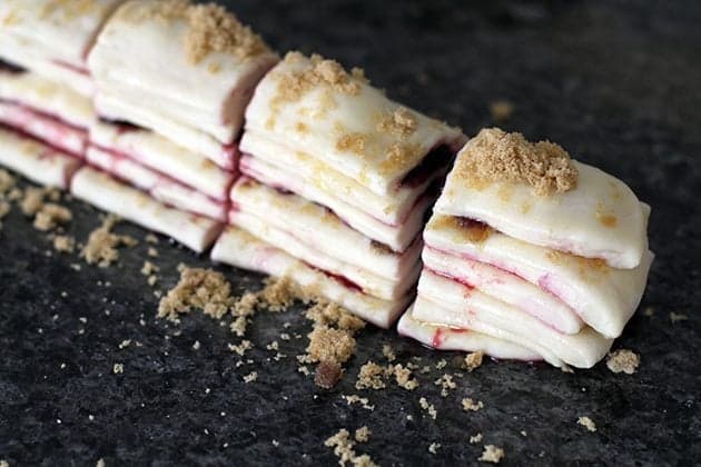 sliced stack of dough strips with sprinkled sugar and halves cherry in between