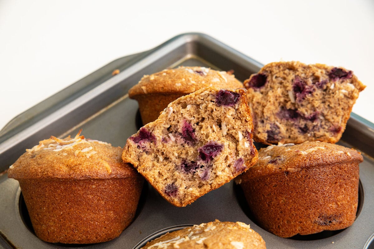 cherry coconut whole wheat muffins pulled out of a muffin tin propped on top one cut in half.