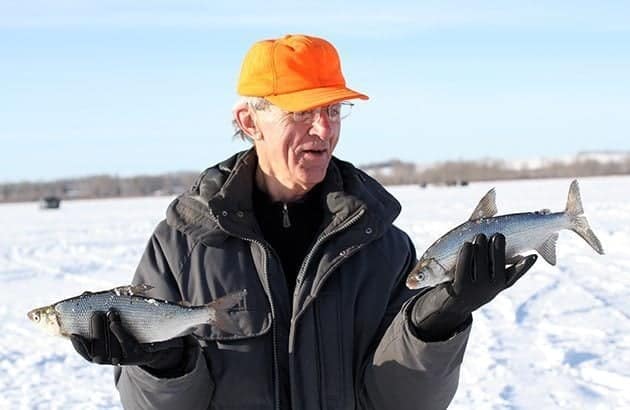 man wearing orange cap and black jacket holding fish, one in each hand