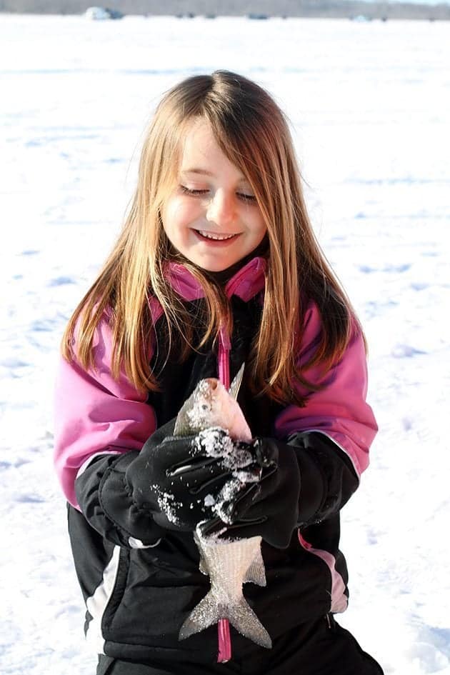 young girl looking down to the fish that she's holding with both hands