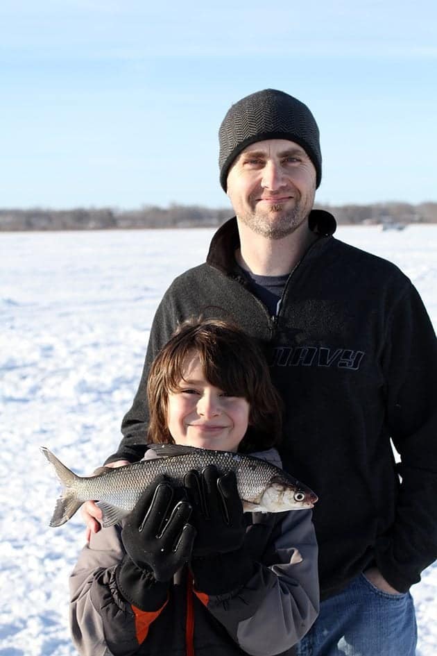 child holding his newly caught fish with his Dad on his back