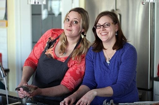 sisters in red and blue blouses with one holding a fish