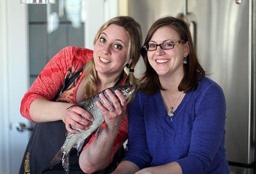 sisters in red and blue blouses with one holding a fish