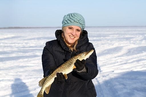 woman in black coat holding a fish during ice fishing at Lac St Anne