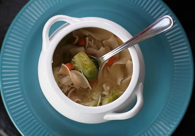 top down shot of Chicken Soup bowl over jade blue plate with spoon on it