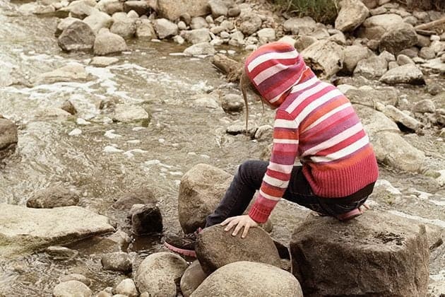 young girl sitting in a big rock with her feet on the water on creek