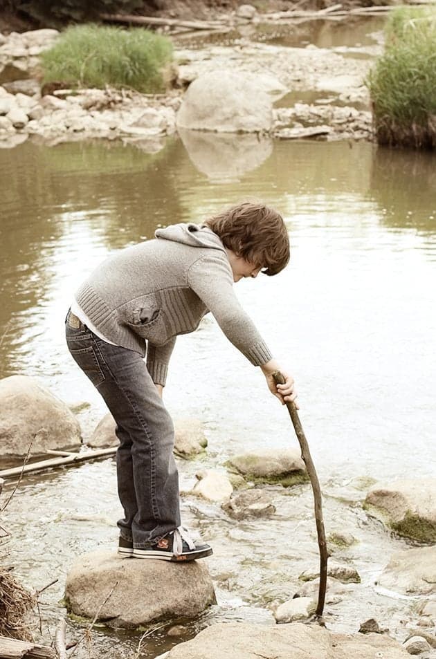 young boy using the wood stick on the water in the creek